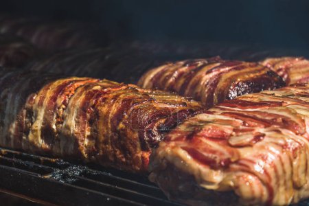 Foto de Primer plano de la carne con tocino preparado en una gran barbacoa fumador en un festival público. Copiar espacio. - Imagen libre de derechos