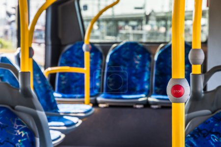 Stop-Taste im modernen Bus des öffentlichen Verkehrs. Leerer Businnenraum. Öffentliche Verkehrsmittel in der Stadt. Personenbeförderung. Bus mit blauen Sitzen und gelben Geländern.