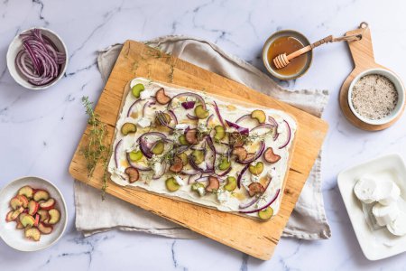 Photo for Tarte flambee with rhubarb, red onions, goat cheese and honey, prepared for baking, marble background, top view - Royalty Free Image