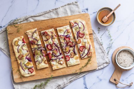 Foto de Flambee tarta al horno con ruibarbo, cebollas rojas, queso de cabra y miel, cortado en tiras, fondo de mármol, vista superior - Imagen libre de derechos