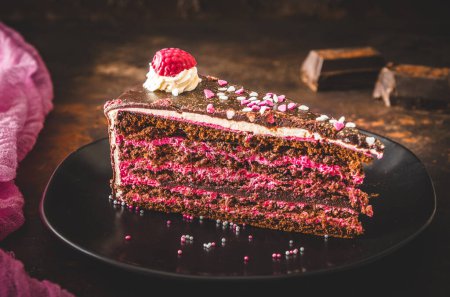 Piece of raspberry chocolate torte on a black plate on dark brown background