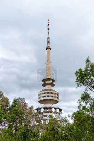 Foto de Fotografía de la parte superior de una gran torre de telecomunicaciones rodeada de árboles contra un cielo gris nublado en Australia regional - Imagen libre de derechos
