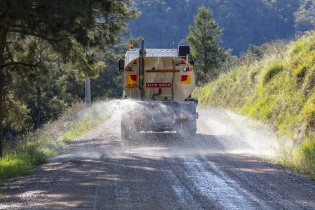 Photo for Photograph of a large water tanker spraying water on a dirt road that is under repair running through a forest to reduce dust in the Blue Mountains in regional Australia - Royalty Free Image