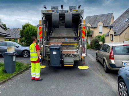 Foto de Caen, Francia 2022. Camión recolector de basura, de pie junto a un trabajador de chalecos amarillos en el trabajo en una urbanización unifamiliar en Caen - Imagen libre de derechos