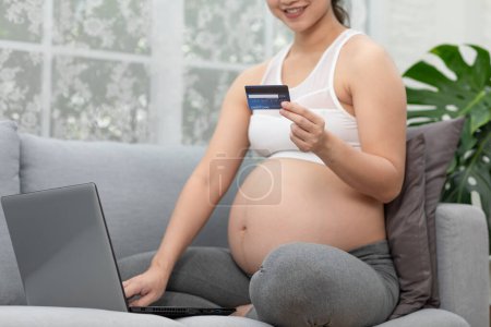 Photo for Happy pregnant woman using credit card shopping online at home.Mother purchasing baby clothes from internet online store by Computer laptop.Pregnancy Shopping Online Concept - Royalty Free Image