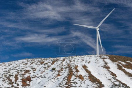 Foto de Turbinas eólicas en una granja de molinos de viento para la producción de energía alternativa que se muestra en las montañas Tehachapi cubiertas de nieve en el sur de California. - Imagen libre de derechos