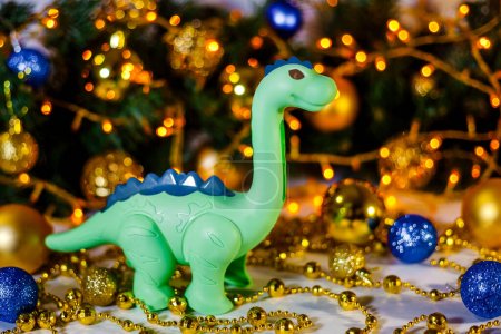 Green dragon on Christmas background. New Year's background of a Christmas tree and a golden garland. Dinosaur. Greeting card. Space for text. Chinese New Year. Christmas, New Year