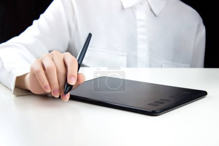 Foto de Una joven trabaja en una tableta gráfica inalámbrica, sosteniendo un bolígrafo en una mano. - Imagen libre de derechos