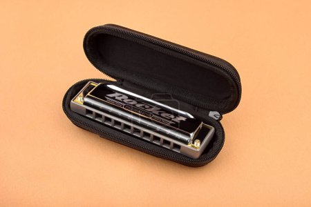 Téléchargez les photos : Hohner professionnel diatonique Rocket harmonica se trouve dans un boîtier noir ouvert. Sur un fond brun clair - en image libre de droit