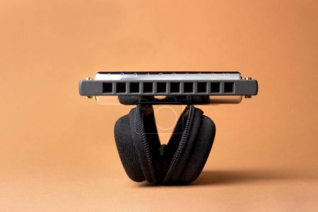 Téléchargez les photos : Un harmonica professionnel repose sur un boîtier noir ouvert, avec des trous dans le cadre. Sur un fond brun clair - en image libre de droit