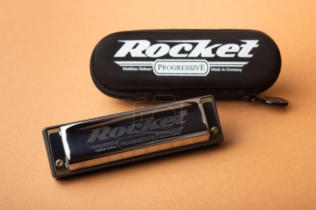 Téléchargez les photos : Un harmonica professionnel Hohner Rocket diatonique à côté de son boîtier noir fermé. Sur un fond brun clair - en image libre de droit