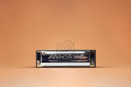 Photo for The Hohner Rocket professional diatonic harmonica stands at the forefront.  On a light brown background - Royalty Free Image