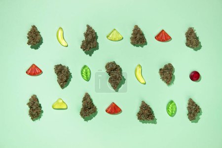 Foto de Brotes secos de marihuana medicinal se encuentran en orden mezclado con dulces masticables en un fondo de menta. Vista superior, ahorrar espacio, caramelos de goma - Imagen libre de derechos