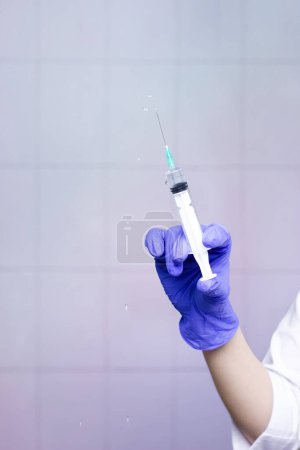 Foto de La mano de una mujer en un guante médico sostiene una jeringa y salpica el medicamento. Sobre un fondo claro - Imagen libre de derechos
