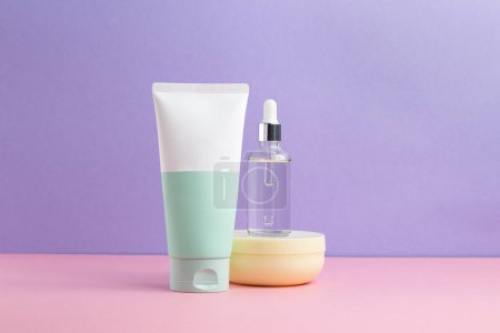 Foto de Productos para el cuidado de la piel, espuma, suero, limpiador. tres productos sobre fondo rosa y lila. Un montón de espacio libre - Imagen libre de derechos