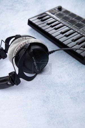 Foto de Los auriculares cerrados de la marca beyerdynamic dt 770 se encuentran junto al teclado midi AKAI MPK mini mk2, sobre un fondo claro - Imagen libre de derechos