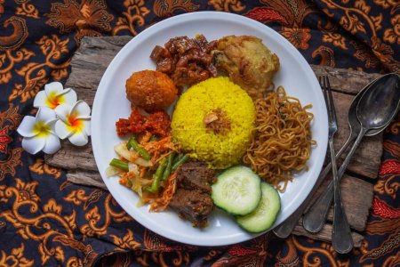 Téléchargez les photos : Indonesian traditional food, nasi kuning / yellow turmeric rice served with beef rendang, fried chicken, vegetables, spicy eggs, noodles, and tempeh - en image libre de droit