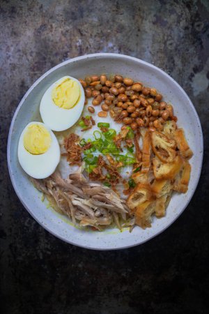 Téléchargez les photos : Bubur ayam, bouillie de riz indonésienne avec poulet râpé et servi avec des œufs durs bouillis, des craquelins de crevettes et du sambal à la pâte de chili - en image libre de droit