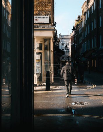 Straßenfoto eines Mannes, der die Straße im Morgensonnenlicht mit dunklen Schatten in London überquert