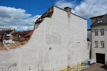 Photo for The half-destroyed high brick wall of the house is slated for demolition. Against the background of the blue sky and another house - Royalty Free Image