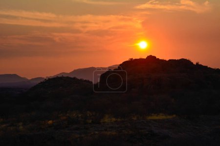 Photo for Evening view of savannah hills with sun setting behind them, crimson sky and shadows - Royalty Free Image