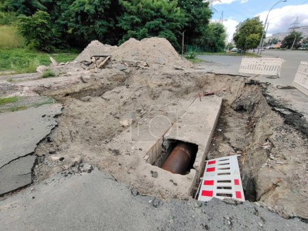 Téléchargez les photos : Un trou est creusé sur la route avec des tuyaux d'égout au fond. Travaux de réparation de routes et d'égouts de mauvaise qualité - en image libre de droit