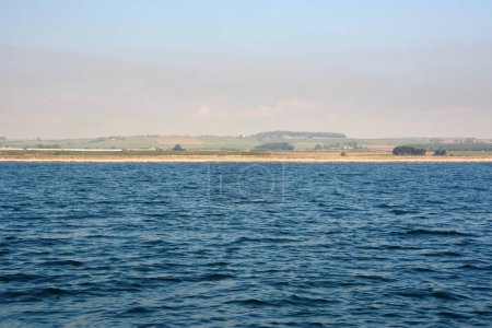 Seascape with distant shore and clear sky. There are fields and parks on the banks
