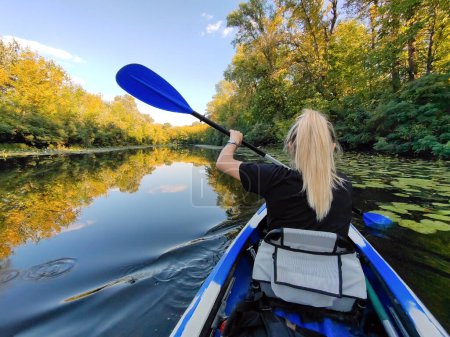 A young blonde woman is paddling in a kayak. Rear view. Tourism, sports and outdoor recreation