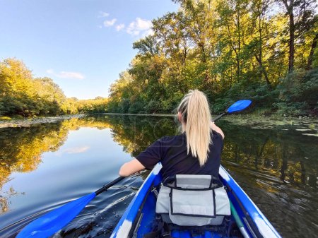 A young blonde woman is paddling in a kayak. Rear view. Tourism, sports and outdoor recreation