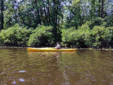 Un adolescente está navegando en kayak por el río en un chaleco salvavidas y haciendo ejercicio. Vista lateral. Vida deportiva activa y recreación