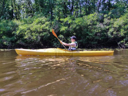 Un adolescent fait du kayak sur la rivière en gilet de sauvetage et de l'exercice. Vie sportive active et loisirs
