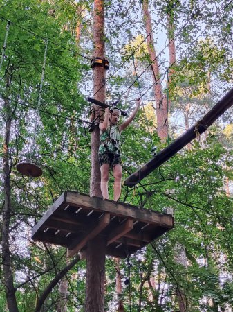 Foto de Un adolescente en un parque de cuerdas en un parque de atracciones se mueve en un puente colgante. Vista desde abajo sobre el fondo de los árboles - Imagen libre de derechos