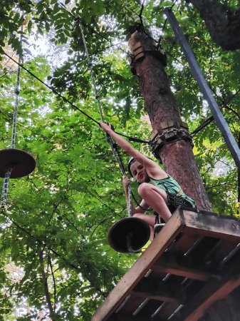 Foto de Un adolescente en un parque de cuerdas en un parque de atracciones se mueve en un puente colgante. Vista desde abajo sobre el fondo de los árboles - Imagen libre de derechos