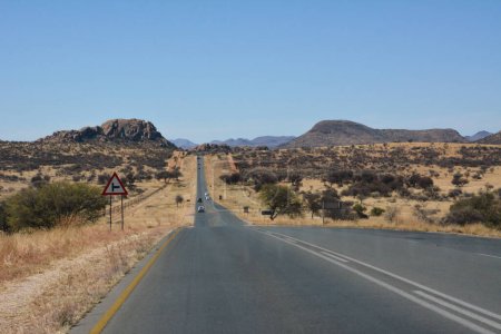 Asphalt road in perspective in desert under clear blue sky. The road leads to distant mountains and hills