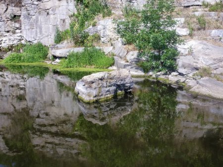 Rocky slopes of a quarry filled with water in which grass and stones are reflected. Natural landscape of beautiful places