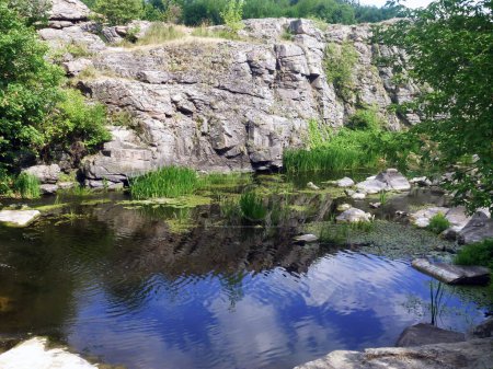 The stony slopes of the former quarry were filled with water and a lake was formed. Grass and stones are reflected in the water. Natural landscape of beautiful places