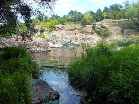 Une petite rivière coule entre les rochers pittoresques, sur les rives desquels les baigneurs de soleil d'apparence méconnaissable reposent sur des pierres