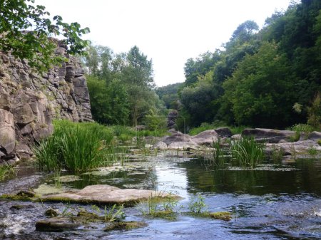 The stony slopes of the former quarry were filled with water and a lake was formed. Grass and stones are reflected in the water. Natural landscape of beautiful places