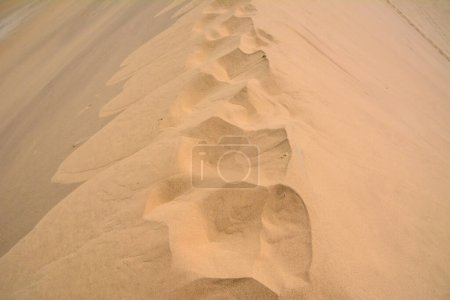 Auf dem trockenen Sand der Wüste sieht man die Abdrücke von jemandes Füßen. Ansicht von oben. Heiße Sommerlandschaft