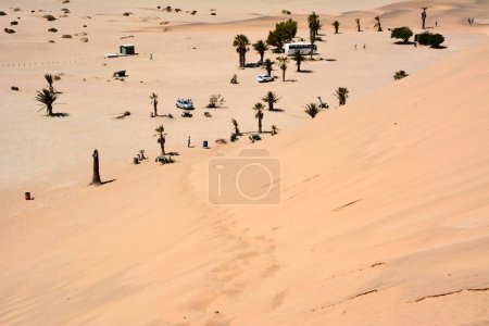 Blick von der Sanddüne auf Wüstenlandschaft und Palmen der Oase mit Touristen Rastplatz unter dem Himmel und Transport. Klima und Austrocknung des Planeten beseitigen