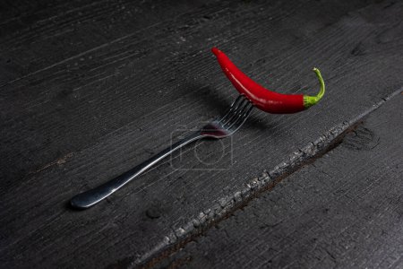 A red chili pepper on a fork on a black table.