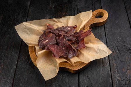 Dried beef jerky on a wooden board on a black wooden background