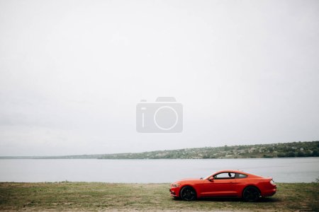 Roter Sportwagen vor dem Hintergrund eines Sees und einer wunderschönen Landschaft