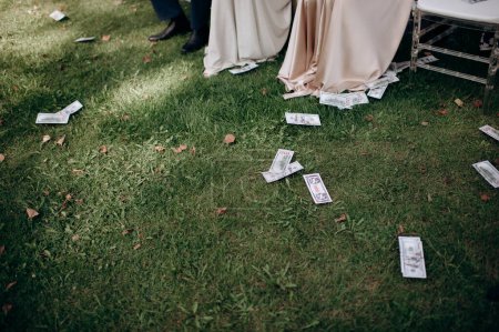 Fake money scattered on the grass at the feet of expensively dressed girls. Throwing money to the wind