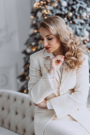Foto de Joven mujer de negocios europea feliz con gafas sentadas en el lugar de trabajo con árbol de Navidad decorado detrás, mujer sonriente que trabaja en la oficina en casa durante las vacaciones de invierno. Enfoque selectivo suave. - Imagen libre de derechos