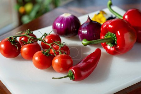 Foto de El tomate rojo, el pimentón, el chile y la cebolla verde, cultivan verduras orgánicas en una tabla de cocción. Comida vegetariana saludable. Nutritionology. Enfoque selectivo suave. - Imagen libre de derechos