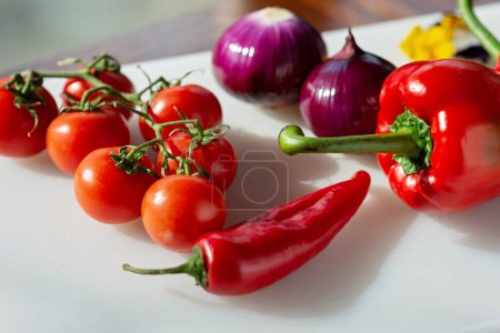 Foto de El tomate rojo, el pimentón, el chile y la cebolla verde, cultivan verduras orgánicas en una tabla de cocción. Comida vegetariana saludable. Nutritionology. Enfoque selectivo suave. - Imagen libre de derechos