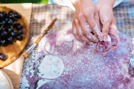 Téléchargez les photos : La main des personnes crée de l'art avec un ingrédient violet, peut-être un fruit, sur la table. Leurs gestes suggèrent qu'ils suivent une recette ou expérimentent la cuisine. Mochi asiatique dessert - en image libre de droit