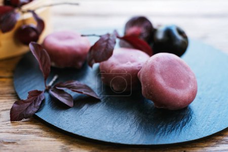 Téléchargez les photos : Assiette de vaisselle noire ornée de boules de fruits violets et de feuilles, servant d'ajout magnifique et naturel à une présentation culinaire ou un geste culinaire. Mochi asiatique dessert - en image libre de droit