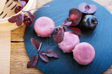 Photo for Purple plums arranged on a stylish black plate resting on a rustic wooden table, creating a beautiful display of fruit and wood. Mochi asian dessert - Royalty Free Image